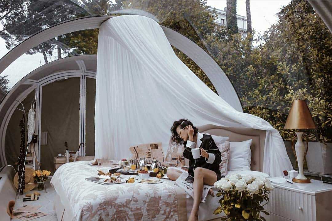 A transparent glamping pod with a girl having breakfast